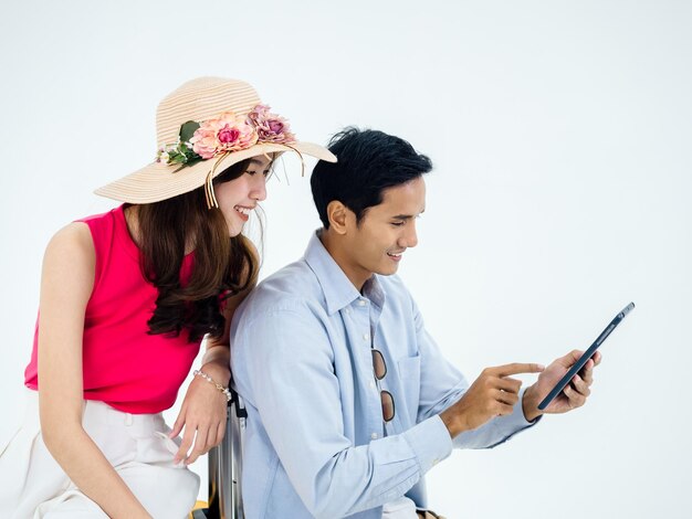 Felice coppia asiatica giovane donna con cappello da spiaggia e uomo in camicia di jeans utilizzando tablet insieme per informazioni di viaggio isolato su sfondo bianco pronto a viaggiare felice vacanza estiva