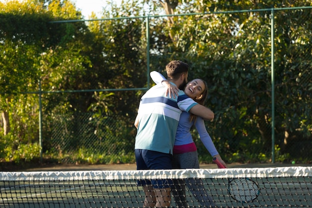 Felice coppia caucasica che gioca a tennis abbracciando il campo da tennis all'aperto