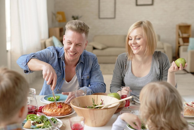 Felice coppia caucasica con bambini che cenano a casa padre che taglia appetitosa torta fatta in casa e sm