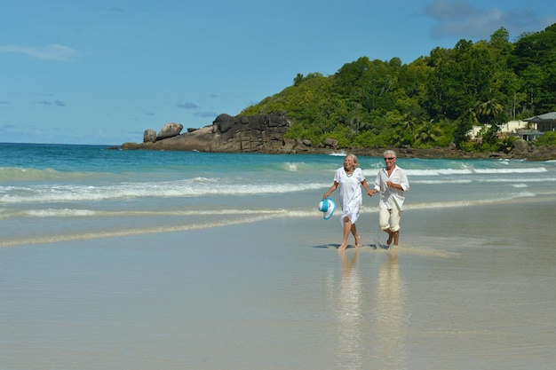 Felice coppia di anziani che cammina sulla spiaggia tropicale