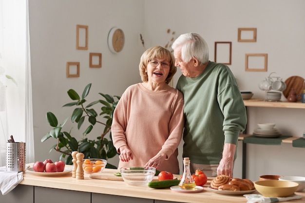 Felice coppia di anziani che si divertono e parlano mentre preparano il cibo insieme in cucina