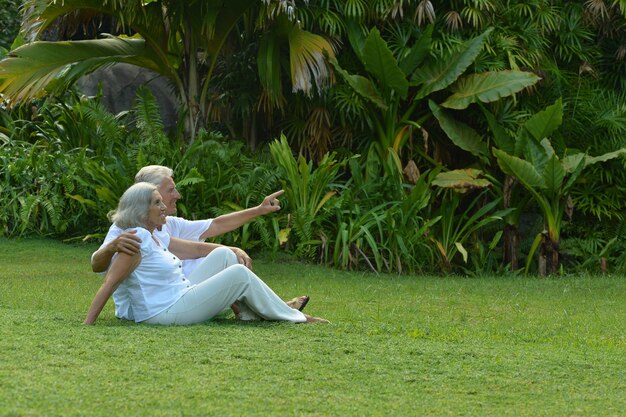 Felice coppia di anziani seduti sull'erba in giardino tropicale all'aperto
