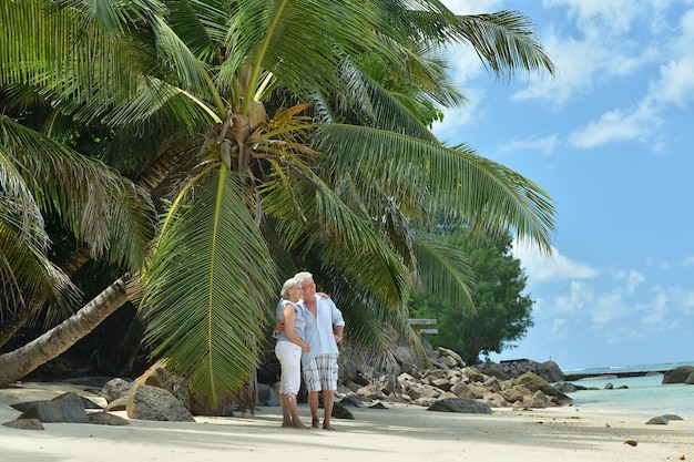 Felice coppia di anziani sulla spiaggia sabbiosa vicino al resort tropicale