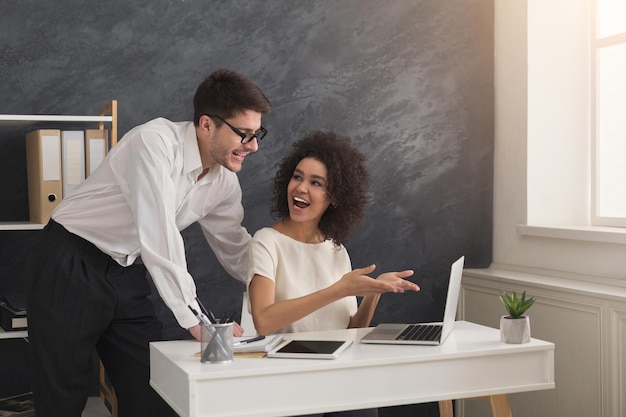 Felice coppia di giovani partner commerciali che lavorano in un ufficio moderno. Due colleghi sorridenti che discutono di un nuovo progetto mentre lavorano al laptop, copia spazio