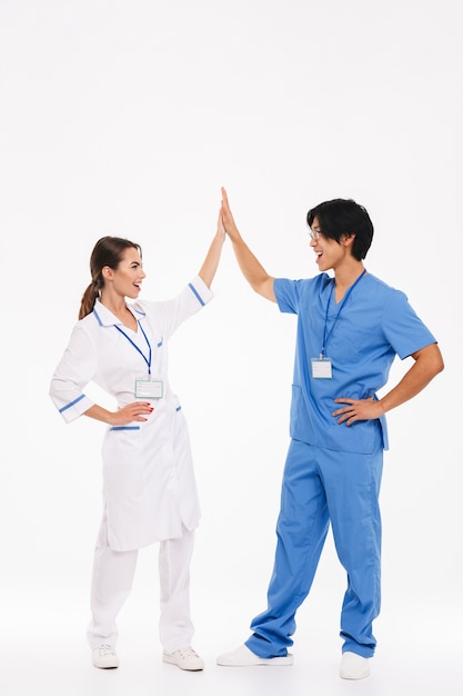 Felice coppia di medici indossando uniforme in piedi isolato su muro bianco, dando il cinque