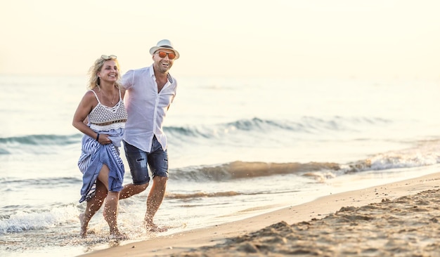 Felice coppia di mezza età innamorata che cammina nell'acqua sulla spiaggia al tramonto