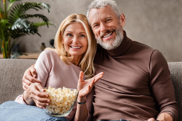 Felice coppia di mezza età moglie e marito guardando la tv e mangiando popcorn