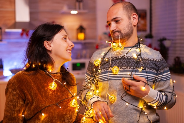 Felice coppia divertita che si infila nelle luci dell'albero di Natale