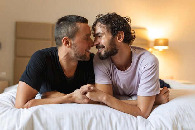 Felice coppia gay sdraiata sul letto a casa abbracciando e flirtando LGBT coppia gay amore momenti concetto di felicità