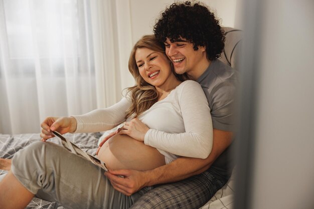 Felice coppia in attesa guardando la scansione medica del loro bambino mentre si rilassa su un letto in camera da letto.