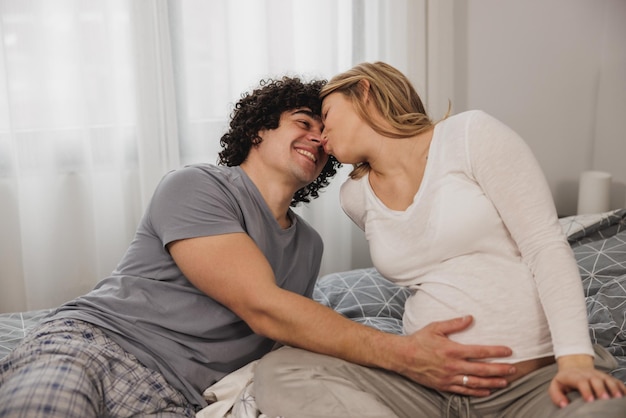 Felice coppia in attesa innamorata che comunica mentre si rilassa su un letto in camera da letto.