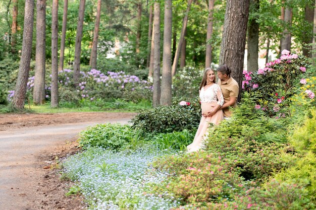 Felice coppia incinta che si abbraccia nel giardino fiorito Futuri genitori nel fiorente parco dei rododendri