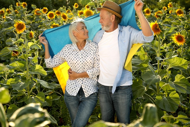 Felice coppia matura con bandiera nazionale dell'Ucraina nel campo di girasoli