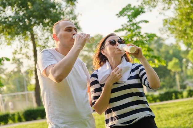 Felice coppia matura nel parco, riposando yogurt da bere, latticini dopo esercizi sportivi