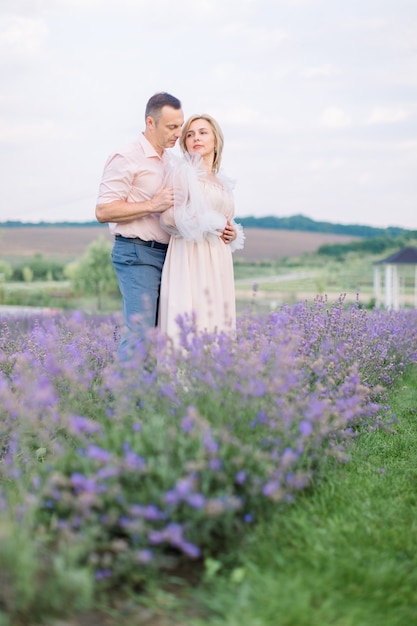 Felice coppia matura romantica innamorata che cammina sul campo di lavanda di fiori viola, in piedi e abbracciata