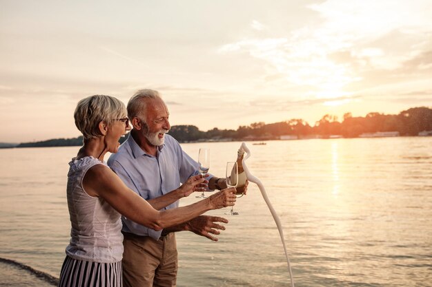 Felice coppia senior che celebra con champagne sulla riva del fiume