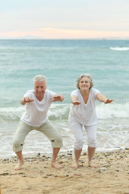 Felice coppia senior che si esercita sulla spiaggia contro il mare