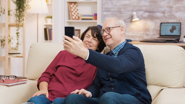 Felice coppia senior seduta sul divano facendo un selfie in soggiorno