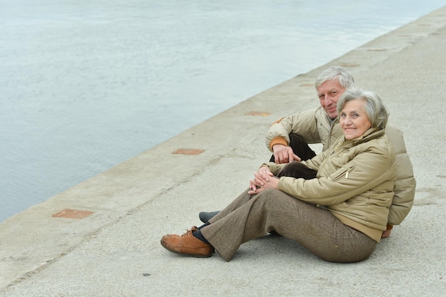 Felice coppia senior vicino all'acqua al parco autunnale