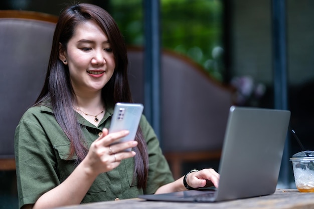 Felice dei freelance asiatici Donna d'affari che scrive un messaggio su smartphone che lavora casualmente con un computer portatile con una tazza da caffè al cafeBusiness Lifestyle