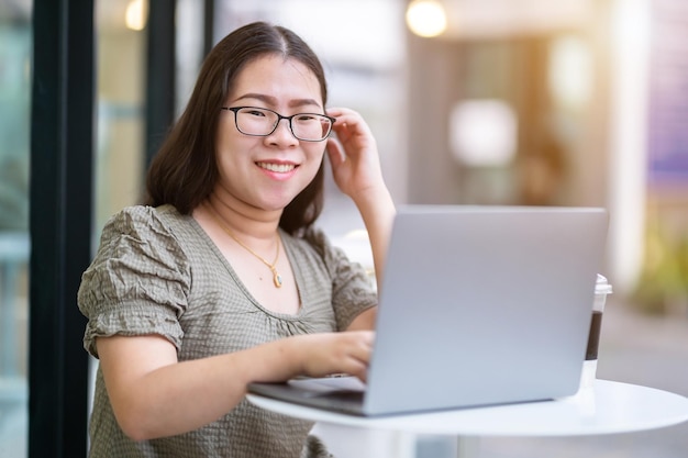 Felice di persone asiatiche freelance business femminile casual che lavora con un computer portatile con una tazza di caffè e smartphone nella caffetteria come il concetto di comunicazione in background