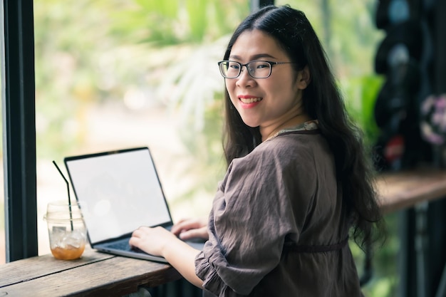 Felice di persone freelance asiatiche business femminile casual che lavora con computer portatile con tazza di caffè e smartphone in caffetteria come lo sfondo, concetto di comunicazione