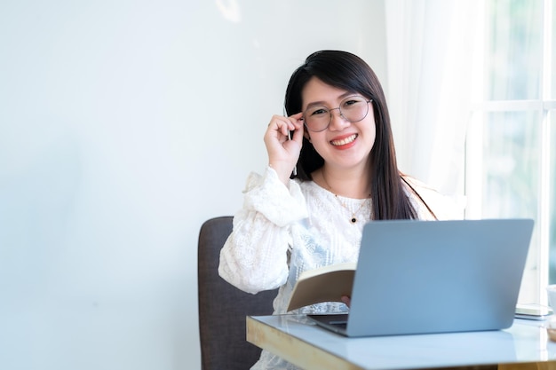 Felice di persone freelance asiatiche Imprenditrice prendendo appunti scritti su un notebook che lavora casualmente con un computer portatile con una tazza di caffè e uno smartphone al caffèBusiness Lifestyle