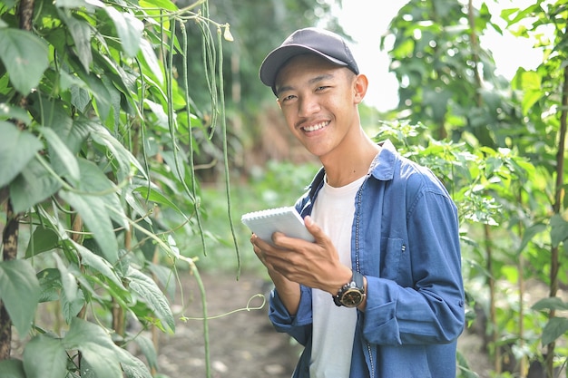 Felice di sorridere giovane agricoltore asiatico maschio tenendo il notebook sul giardino verde, sul posto.