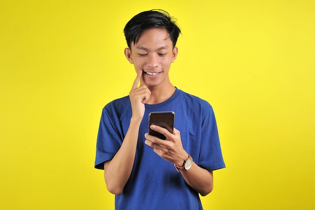 Felice di un giovane uomo asiatico di bell'aspetto che sorride usando lo smartphone isolato su sfondo giallo