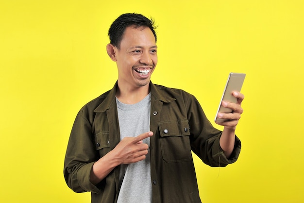 Felice di un giovane uomo asiatico di bell'aspetto che sorride usando lo smartphone isolato su sfondo giallo