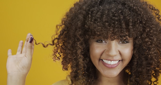 Felice donna africana americana che ride con i suoi capelli ricci su sfondo giallo