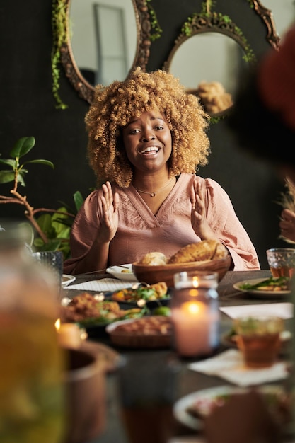 Felice donna africana che batte le mani e celebra qualcosa mentre si siede al tavolo da pranzo