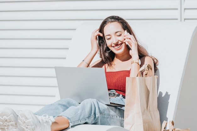 Felice donna africana con uno smartphone o un computer portatile nel centro città che fa shopping al centro commerciale, concetto di stile di vita della donna. Effettuare una chiamata e inviare messaggi durante il riposo dello shopping. Divertirsi in una chiamata, copia spazio