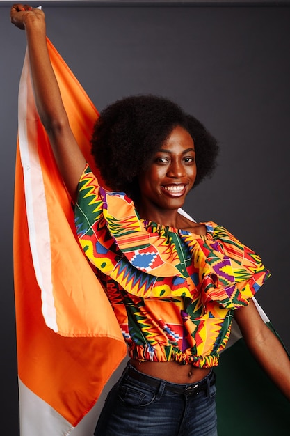 Felice donna africana in abiti nazionali sorridente e in posa con una bandiera Costa d'Avorio C te d'Avoire isolata su uno sfondo grigio