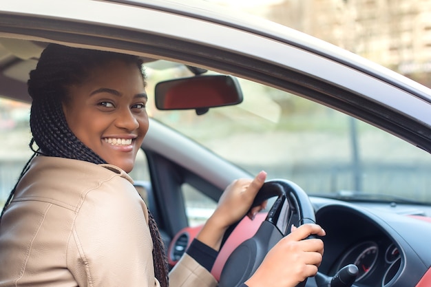 Felice donna afro-americana in un'auto che guida, autunno-inverno.