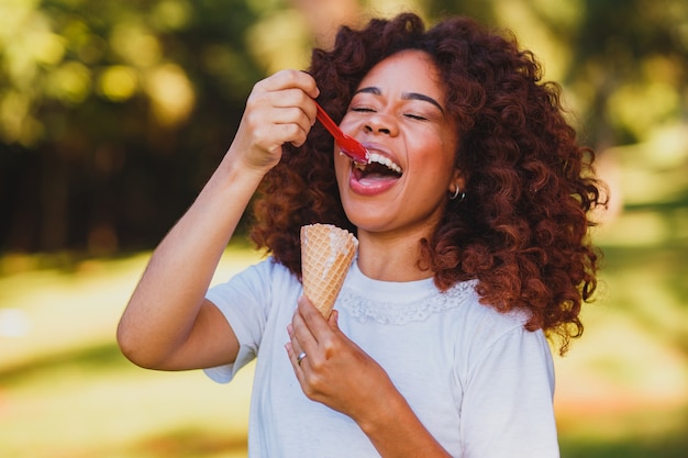 Felice donna afro che mangia il gelato nel parco.