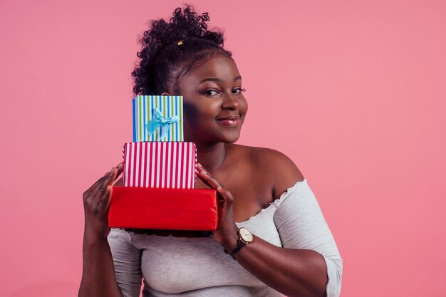 Felice donna afro che tiene scatole regalo 8 marzo in stusio sfondo rosa.
