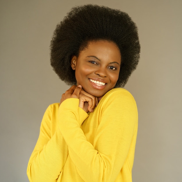Felice donna afroamericana millenaria con stile di capelli afro indossare maglione giallo in posa sopra il muro grigio