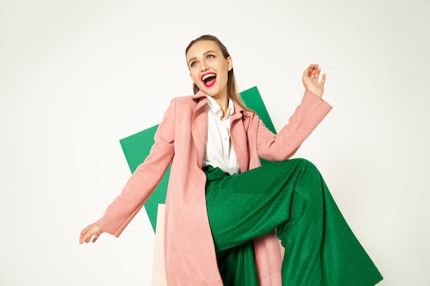 Felice donna alla moda in pantaloni verdi in studio con sfondo bianco