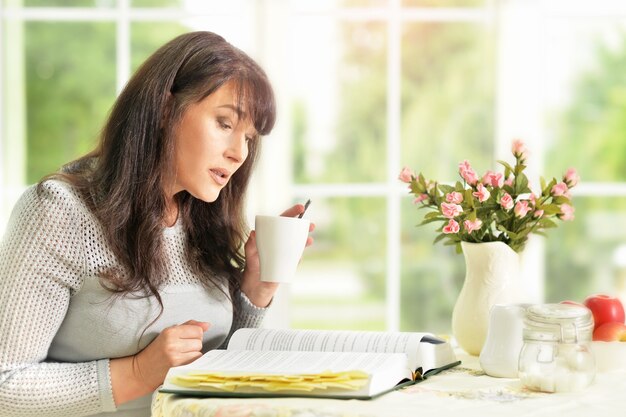 Felice donna anziana che legge un libro con il tè