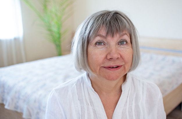 Felice donna anziana con i capelli grigi che si rilassa sorridendo nella sua casa in camera da letto
