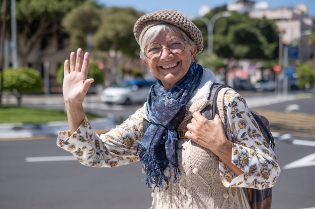Felice donna anziana viaggiatore nel soleggiato centro città che esprime positività buon umore azienda zaino Attraente signora anziana che guarda la fotocamera sorridente