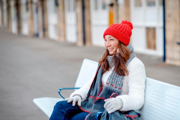 Felice donna asiatica in camice bianco cappello rosso seduto alla stazione e in attesa del treno