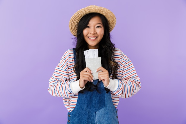 Felice donna asiatica in posa isolato sopra la parete viola che tiene passaporto e biglietti