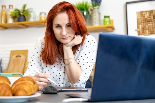 Felice donna attraente lavora al computer portatile in cucina bella donna freelance lavoro a distanza a casa