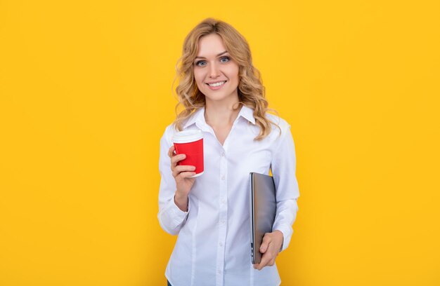 Felice donna bionda con tazza di caffè e laptop su sfondo giallo