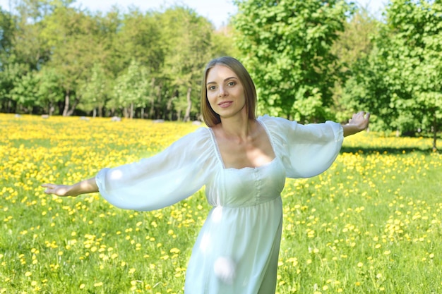 Felice donna bionda in un abito bianco su uno sfondo di un giardino fiorito primaverile con le mani alzate al cielo