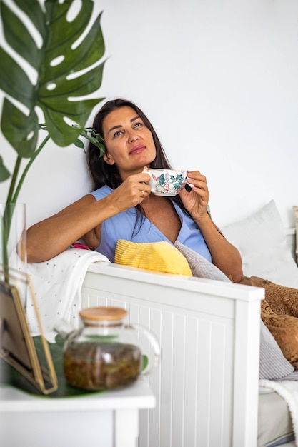 Felice donna bruna elegante rilassata seduta su un comodo divano tazza di tè sognando di passare del tempo da sola