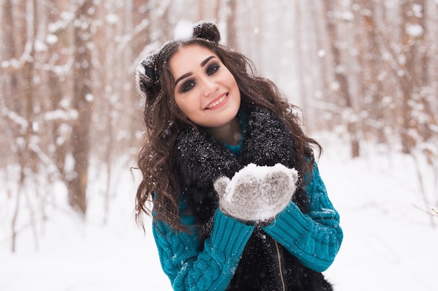 Felice donna bruna in una foresta invernale sorride e tiene la neve nelle sue mani