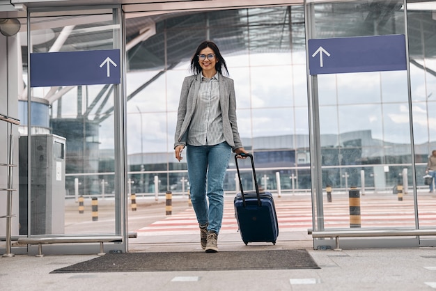 Felice donna caucasica viaggiatrice nel terminal dell'aeroporto con bagagli